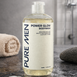 Bottle of Pure Men Power Glow Bodywash on a bathroom counter with a towel and soap bar in the background.