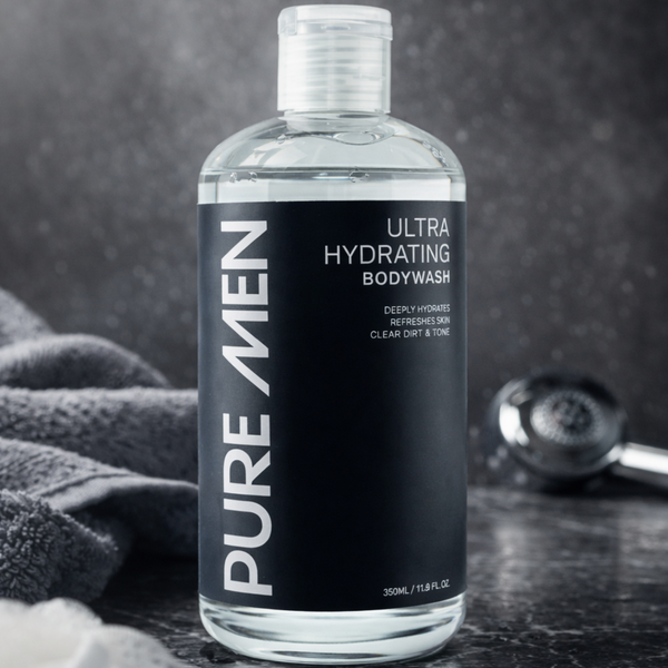 Bottle of Pure Men Ultra Hydrating Bodywash on a dark surface with a towel and soap in the background.